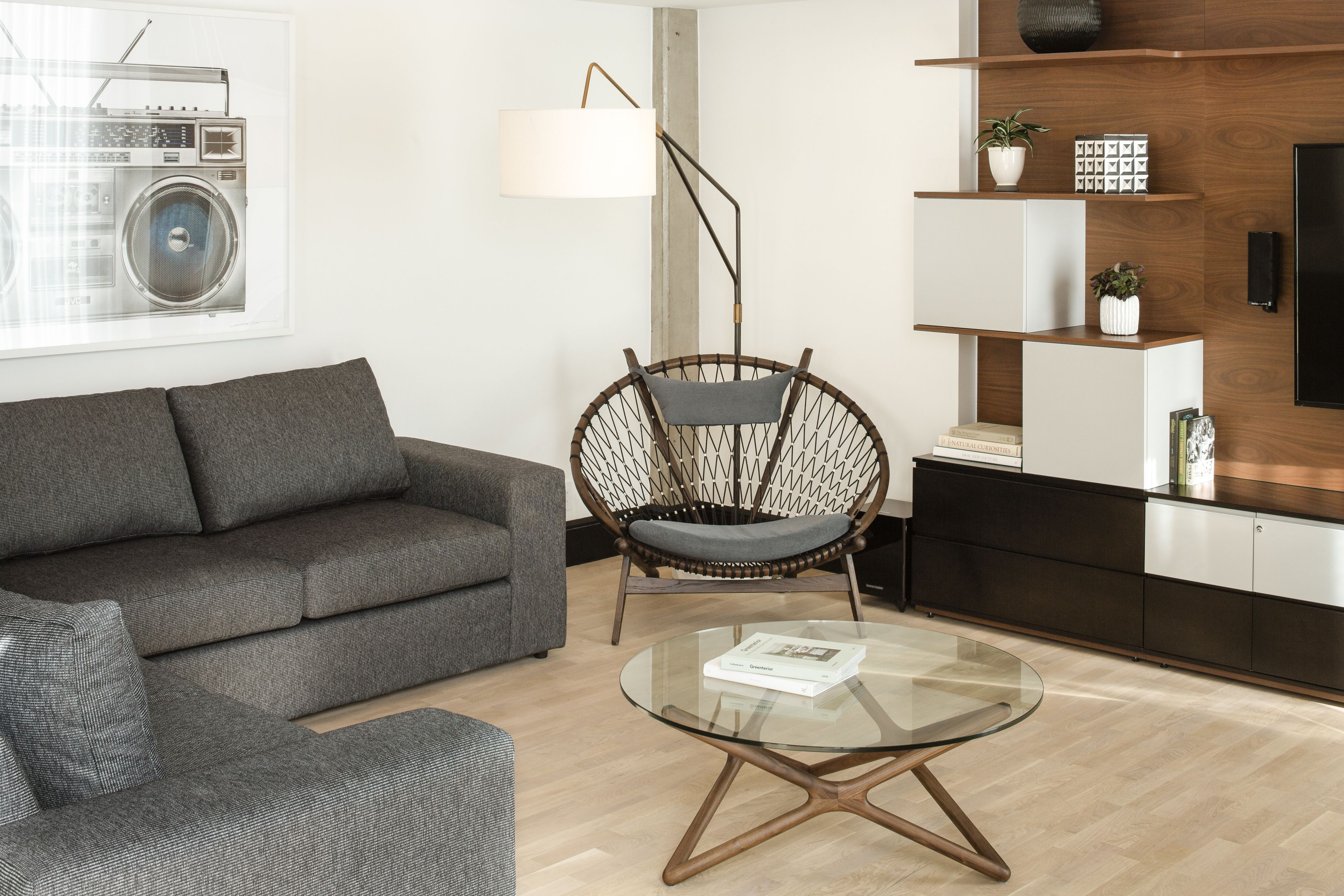 Uma sala de estar moderna com um sofá cinzento, uma poltrona de vime, uma mesa de centro de vidro e um armário de madeira com uma TV.
