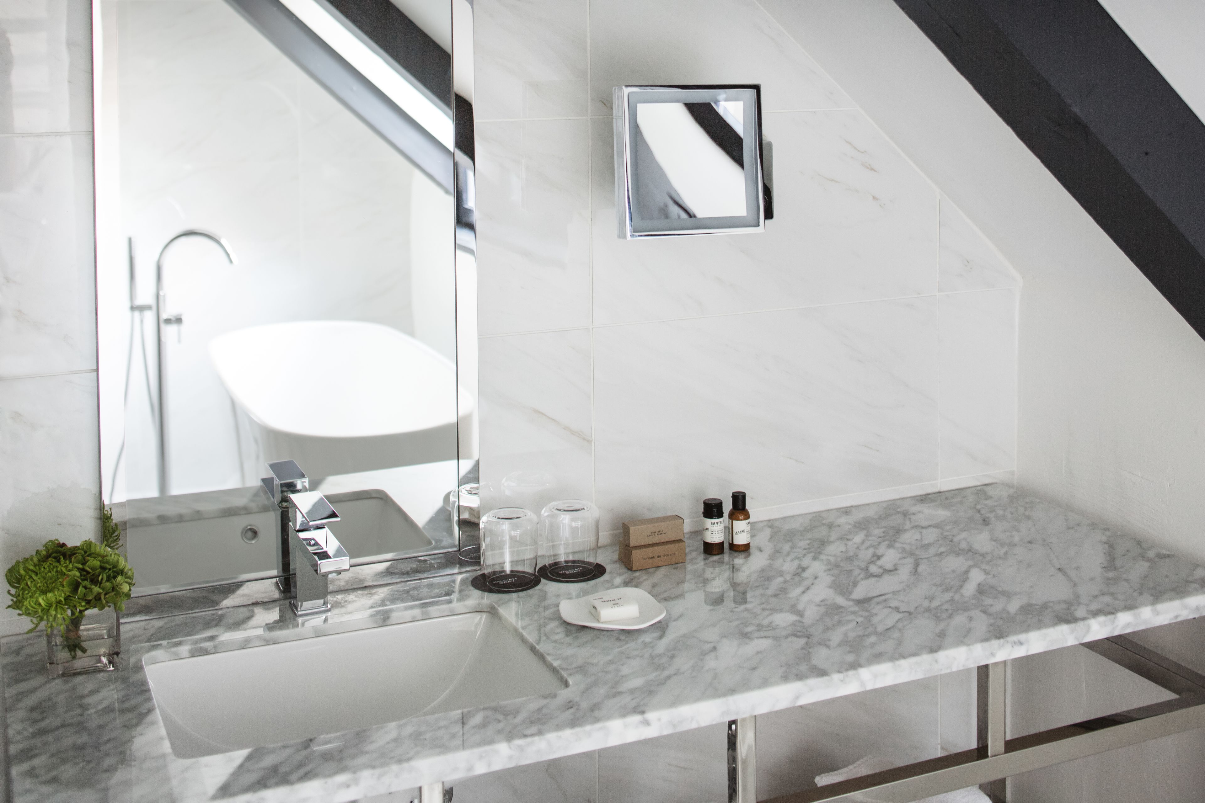 Een moderne badkamer met een marmeren wastafel, een grote spiegel en een douche in de achtergrond.
