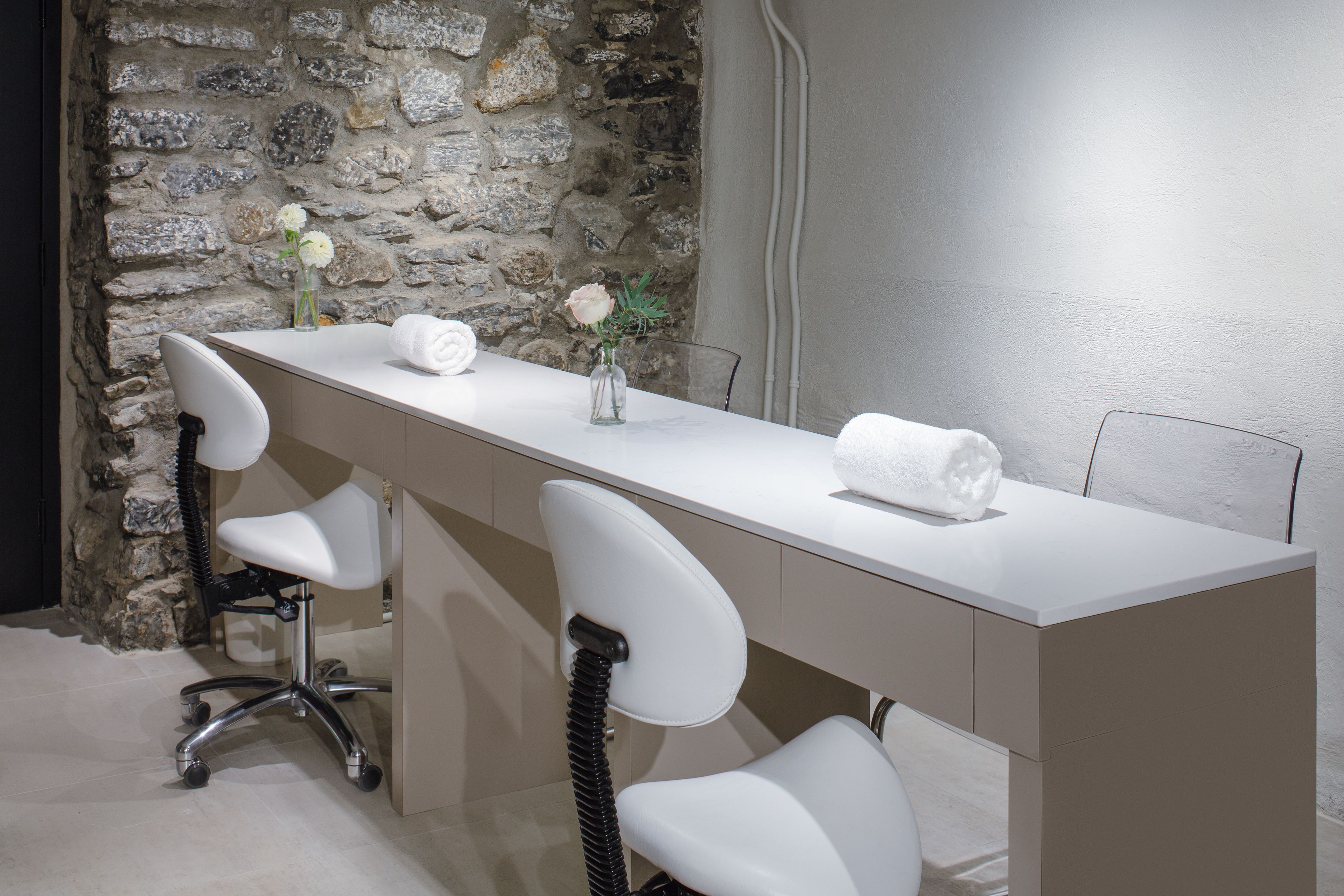 Un baño moderno con pared de piedra, encimera blanca y tres sillas blancas.
