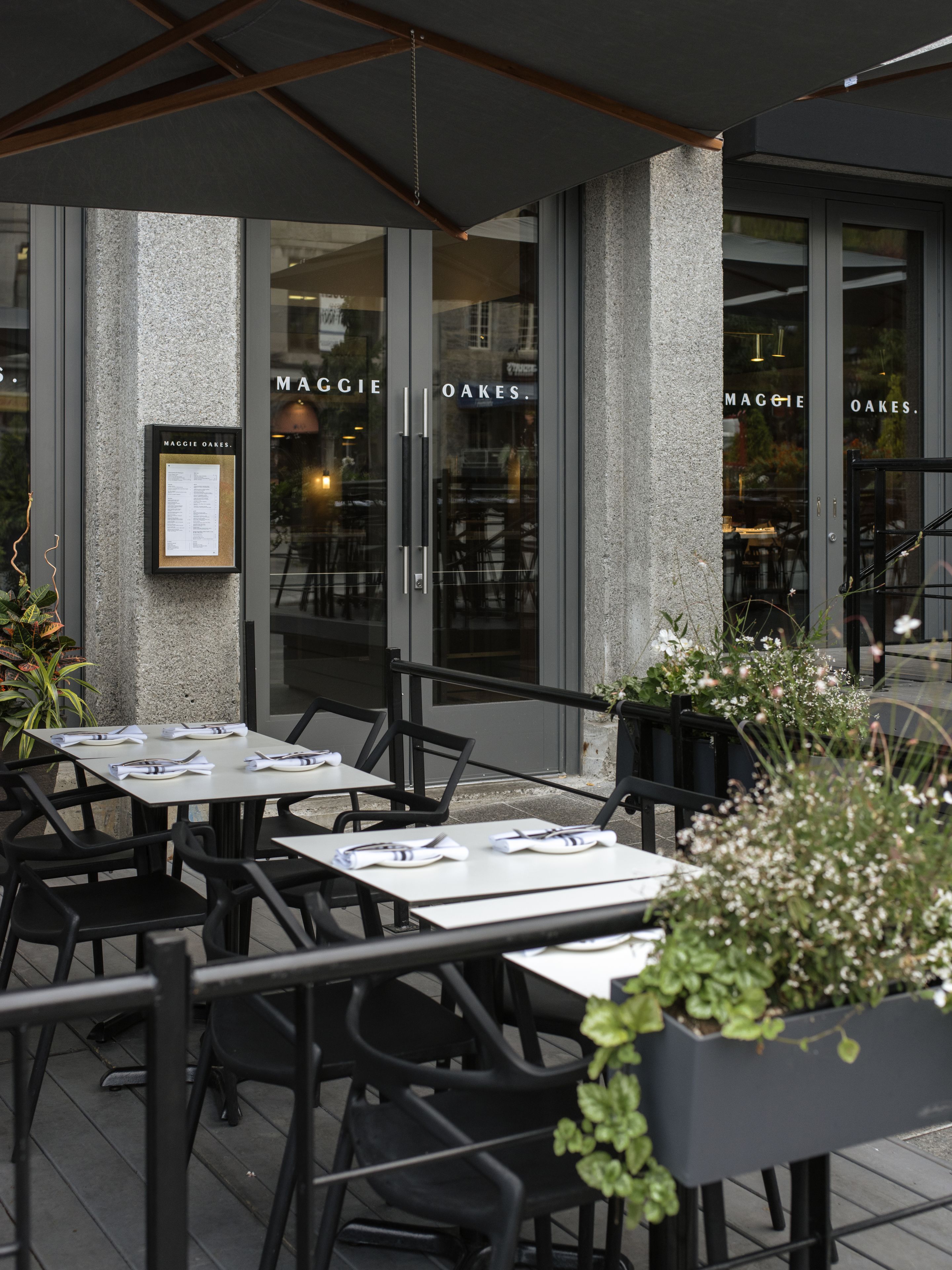 Een terras met tafels en stoelen, een menukaart en een bord met de naam Maggie Oakes.
