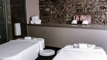Habitación de hotel con dos camas, un taburete pequeño, pared de piedra y cabina de ducha de vidrio.