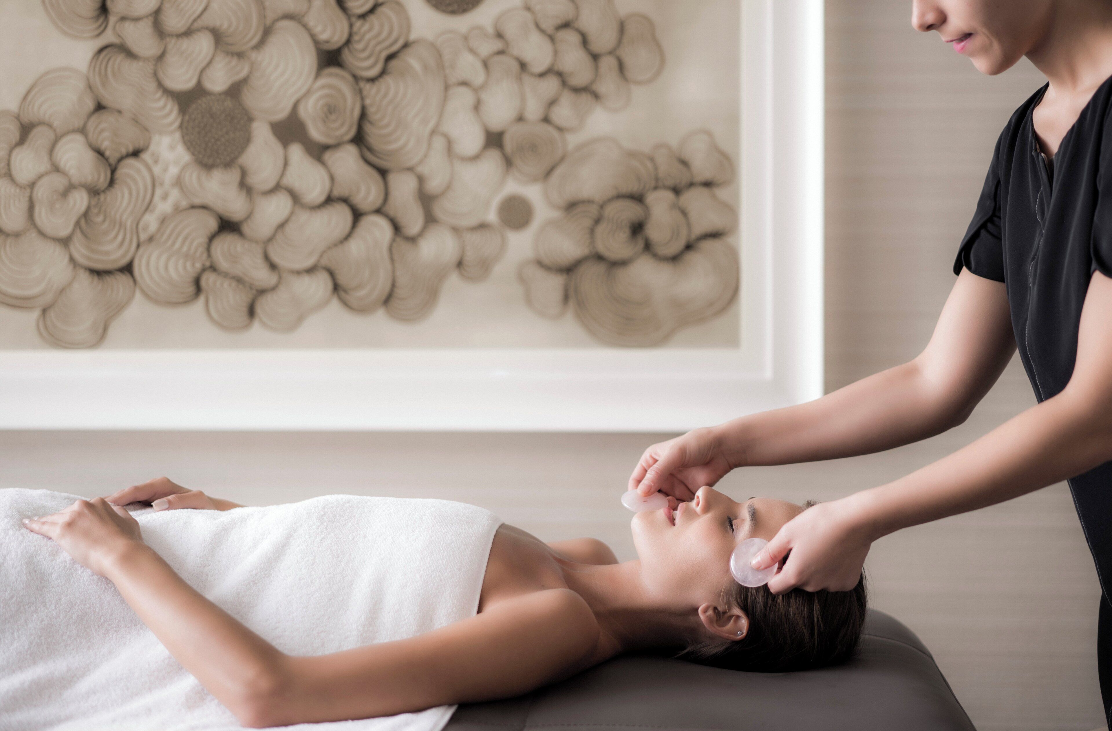 A person lying on a massage table with a towel, receiving a facial treatment.