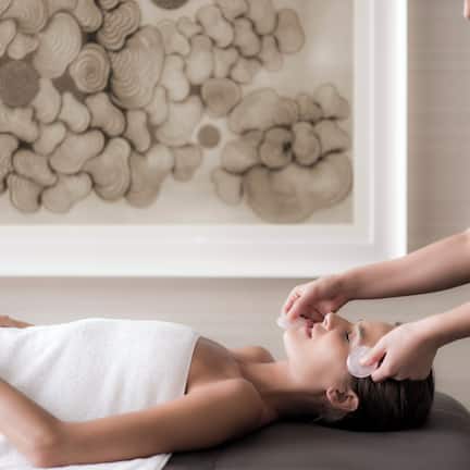 A person lying on a massage table with a towel, receiving a facial treatment.