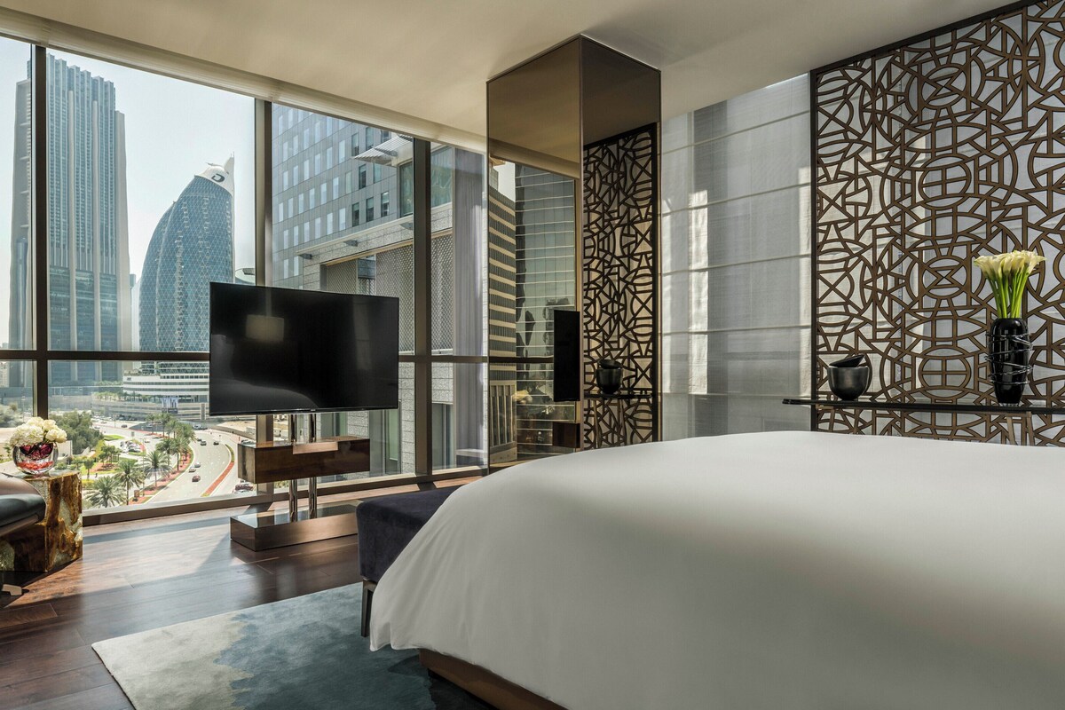A modern hotel room with a large bed, a TV, and a city view.