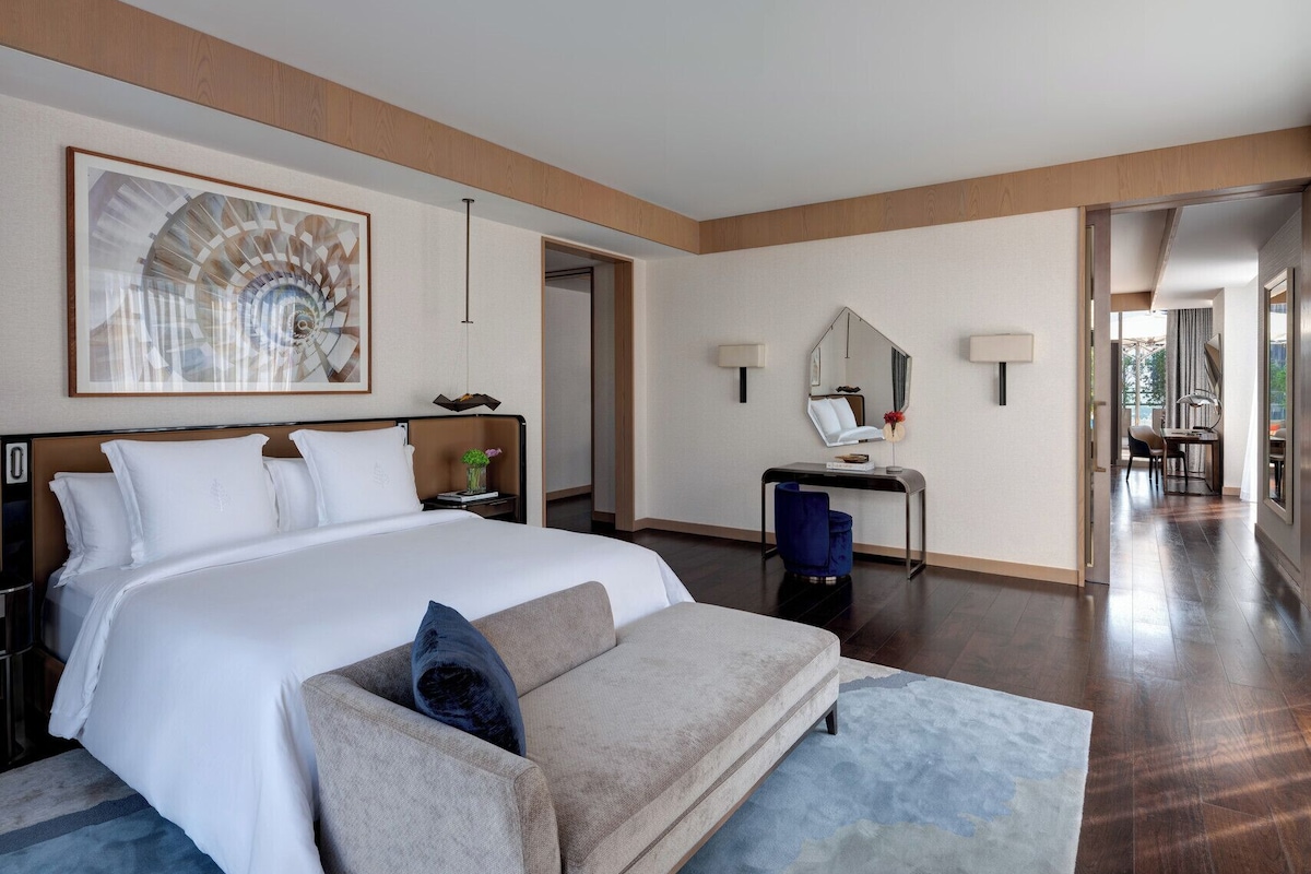 A modern hotel room with a large bed, a desk, a chair, and a mirror.