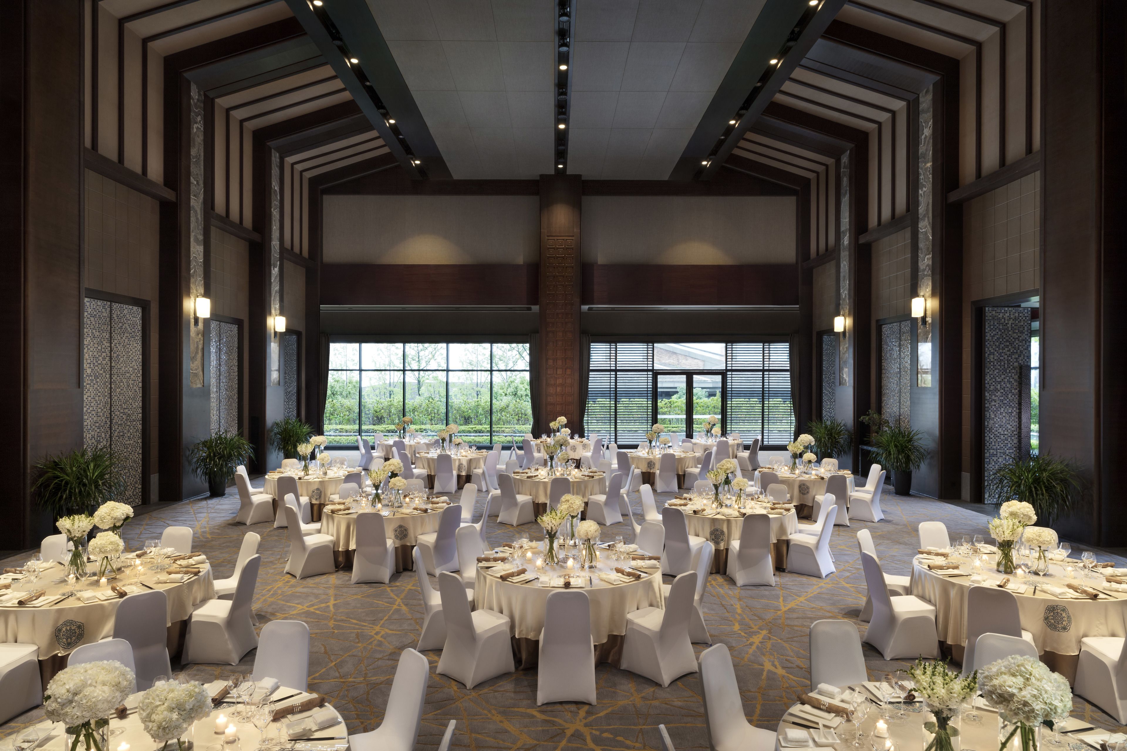 Un amplio salón de banquetes con mesas redondas dispuestas para comer, sillas blancas y centros de mesa florales.