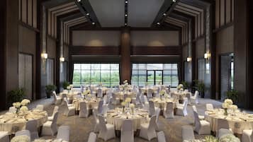 A large banquet hall with round tables set for dining, white chairs, and floral centerpieces.