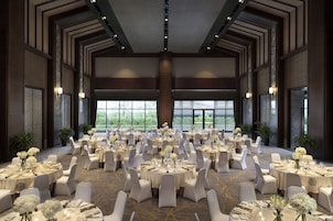 Un amplio salón de banquetes con mesas redondas dispuestas para comer, sillas blancas y centros de mesa florales.