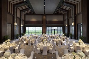 Un amplio salón de banquetes con mesas redondas dispuestas para comer, sillas blancas y centros de mesa florales.