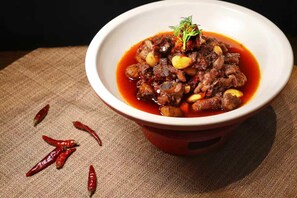 A bowl of stew with a garnish, placed on a textured surface with scattered chili peppers. - Anantara Guiyang Resort (Qiannan)