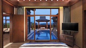 Ein Schlafzimmer mit großem Fenster, Fernseher, Holzkommode und kleinem Pool.