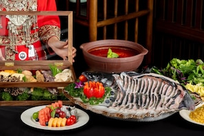 Una mesa con pescado, un tazón de sopa y diversas frutas y verduras.