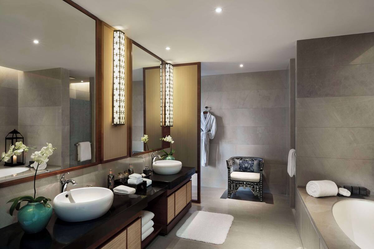 A modern bathroom with two sinks, a large mirror, and a bathtub.