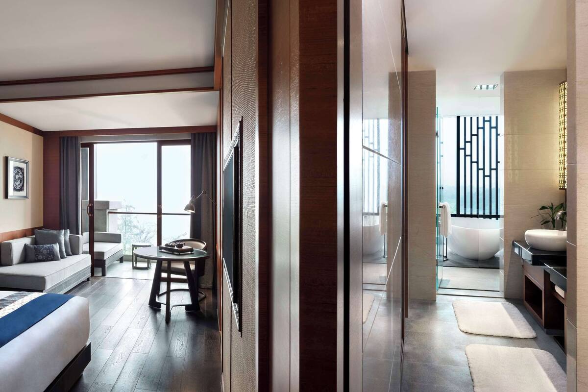 A hotel room with a large bed, a sofa, a small table, and a view of the outside.