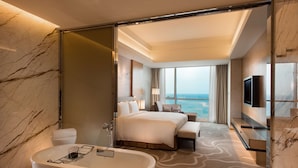 Une chambre d’hôtel moderne dotée d’un grand lit, d’une baignoire, d’une télévision et offrant une vue sur l’océan.