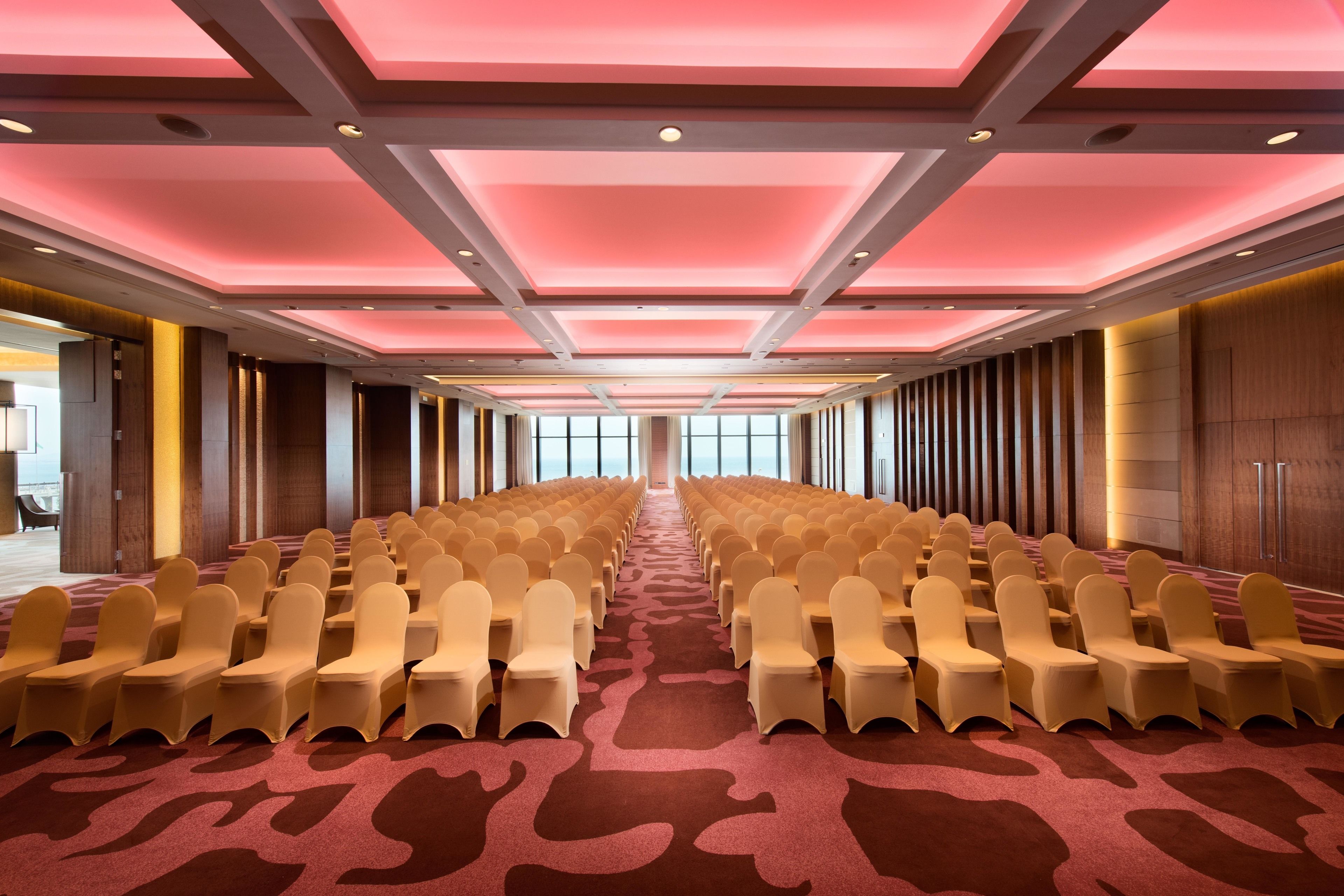 Un salón de conferencias con filas de sillas, una alfombra estampada e iluminación empotrada en el techo.