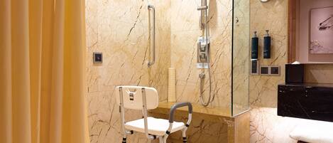 Un baño moderno con suelo de mármol, ducha con cabezal de mano, una silla blanca y un banco negro.
