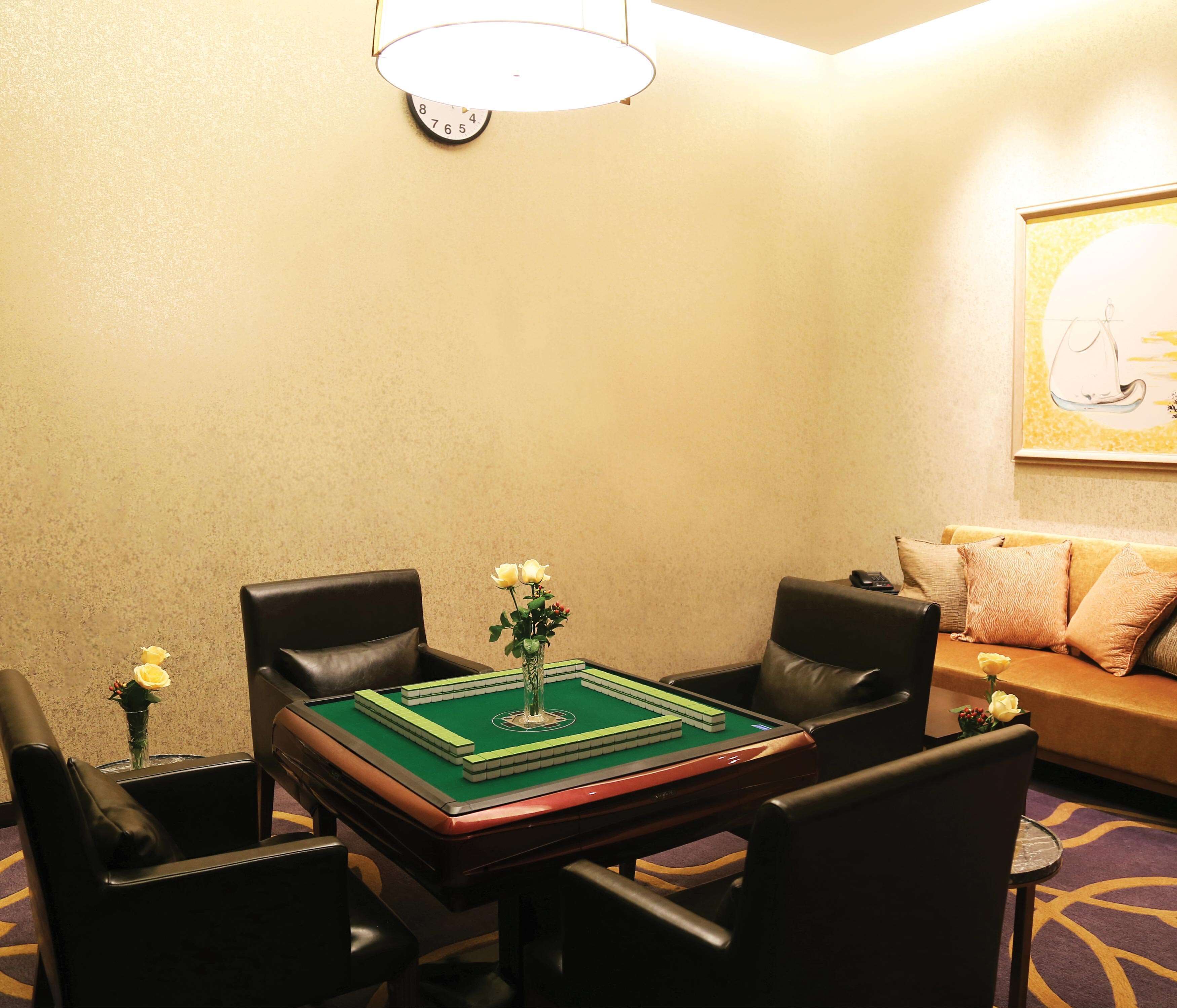 A room with a green felt table for playing cards, a clock on the wall, and a sofa with cushions.
