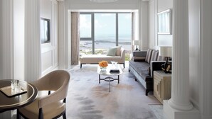 A spacious living room with a large window offering a view of the sea, a sofa, a coffee table with flowers, and a dining area with a chair and a tray. - The Langham, Haikou (Haikou)