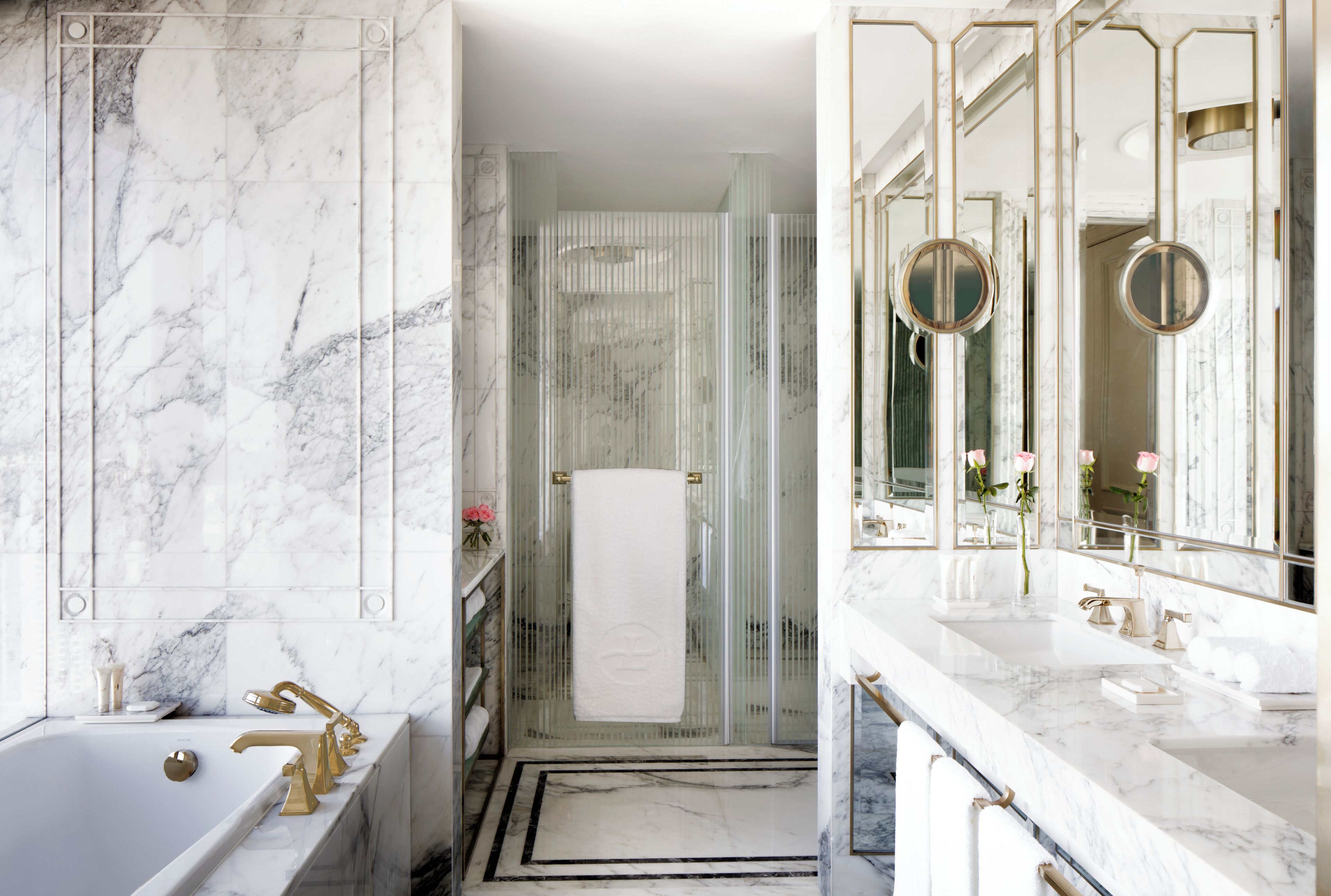 Une salle de bain luxueuse avec un lavabo en marbre, des robinetteries dorées et une douche à parois de verre.