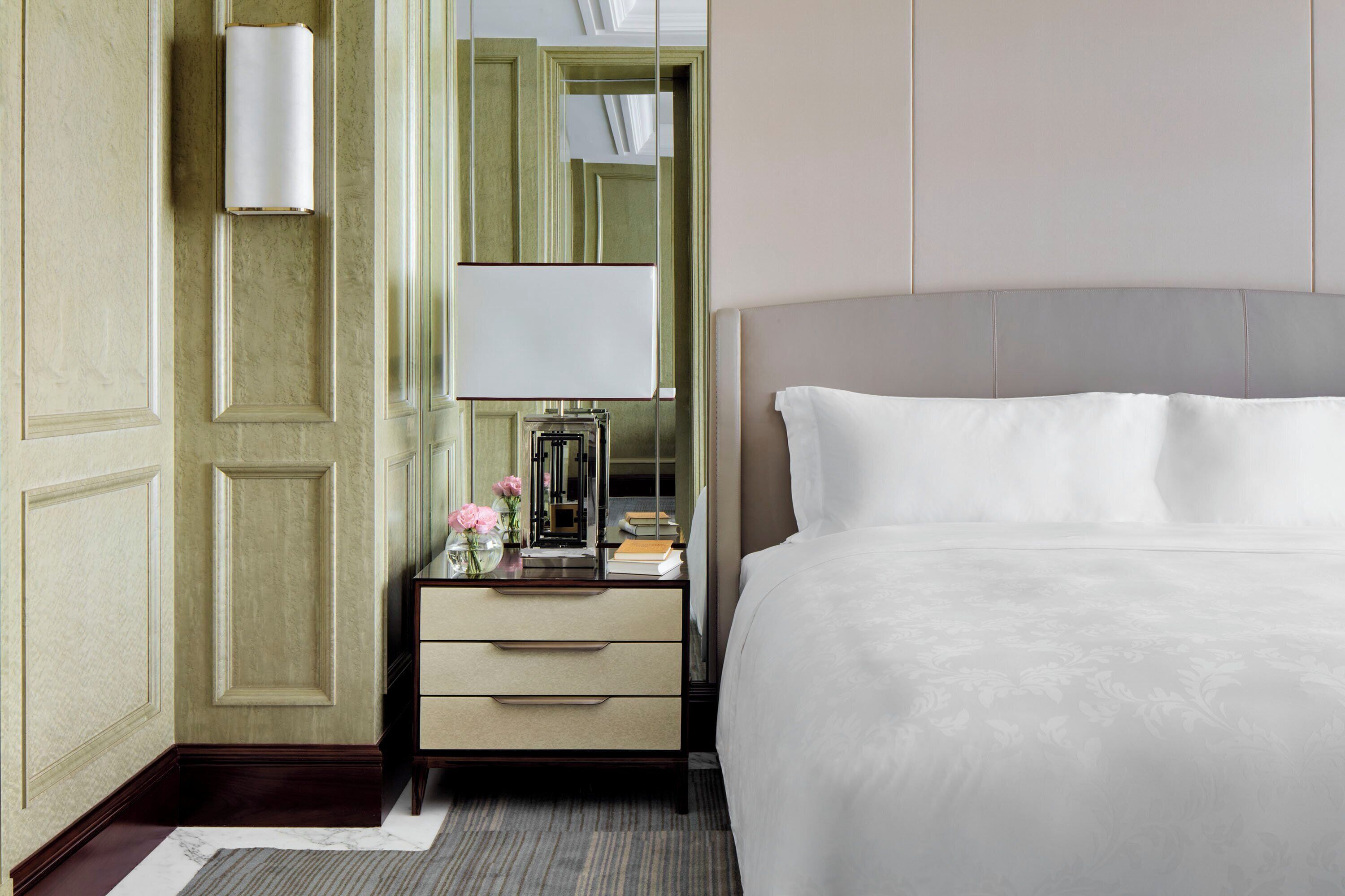 A hotel room with a large bed, a bedside table with a lamp, a mirror, and a dresser.