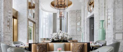Un lobby de hotel lujoso con paredes de mármol, una zona de estar central con una mesa redonda y elegantes candelabros.