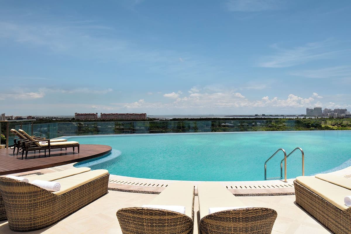 A rooftop infinity pool with lounge chairs and a city view.