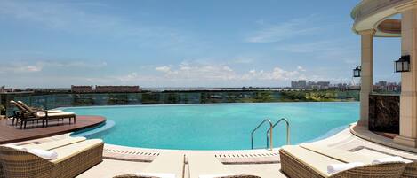 Una piscina infinita en la azotea con sillones de descanso y vistas a la ciudad.