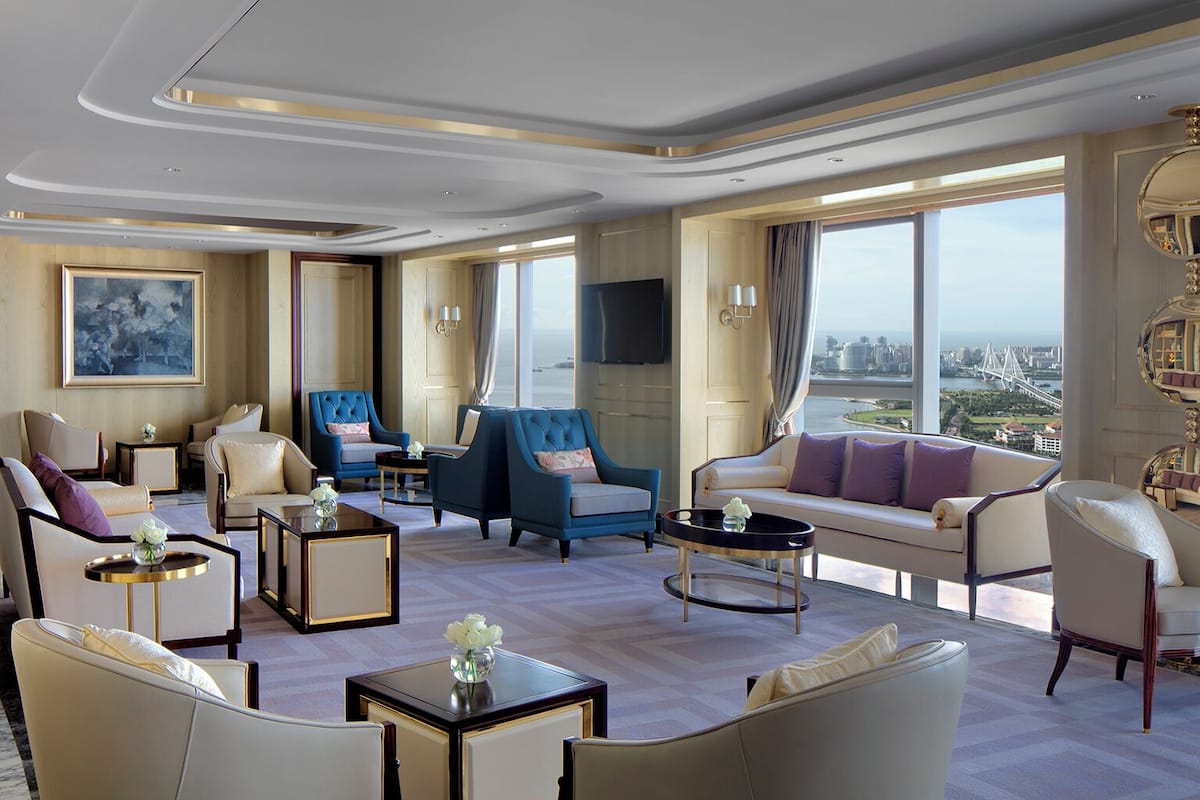 A spacious living room with a large window offering a city view, plush seating, and a modern chandelier.