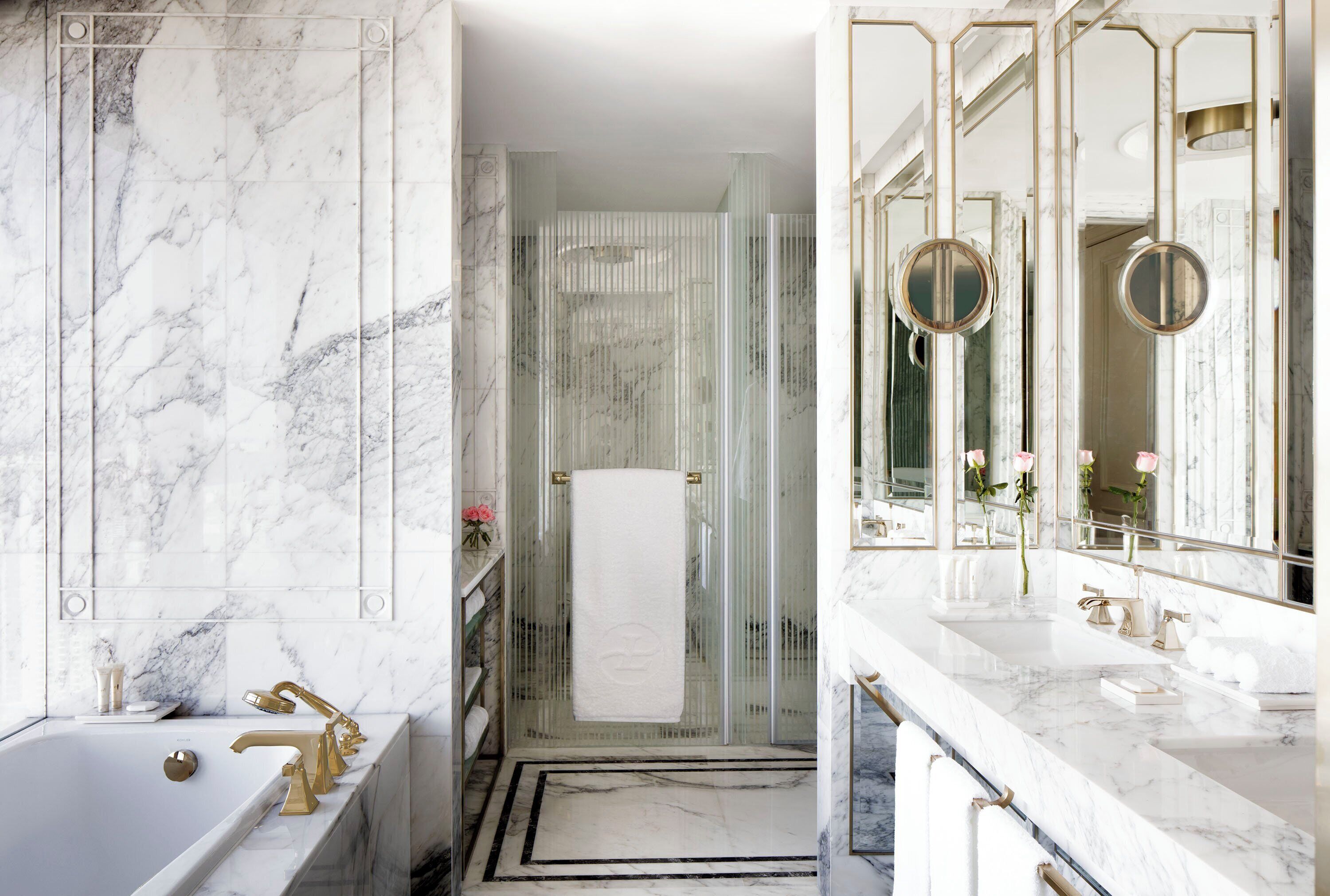 Une salle de bain luxueuse avec une grande baignoire en marbre, un espace douche séparé et un meuble-lavabo doté d’un grand miroir et d’accessoires dorés.