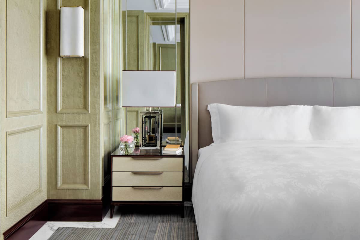 A hotel room with a large bed, a bedside table with a lamp, a mirror, and a dresser.