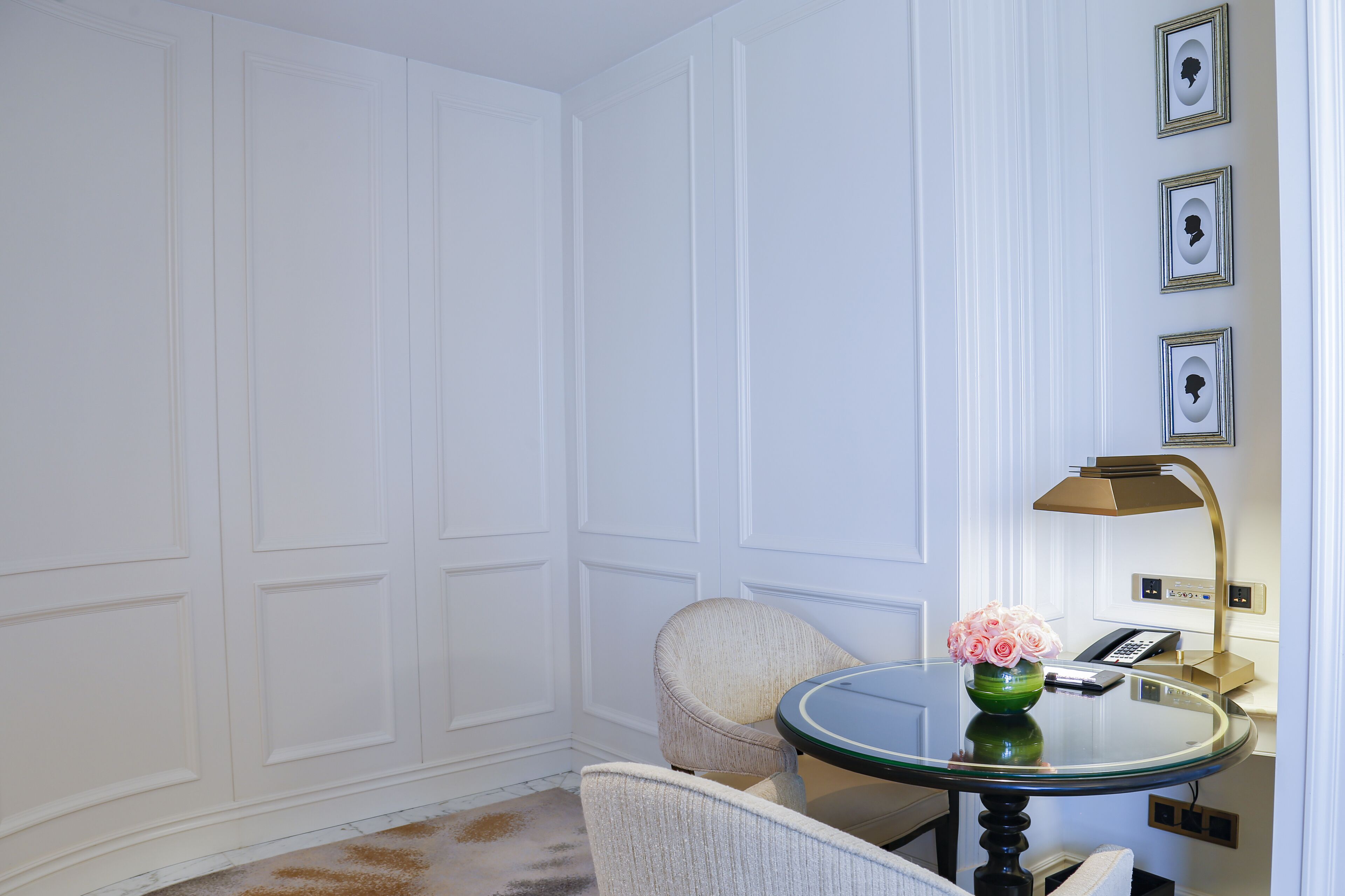 Una habitación con una mesa redonda de vidrio, un jarrón verde con flores, un sillón color beige y una lámpara dorada.