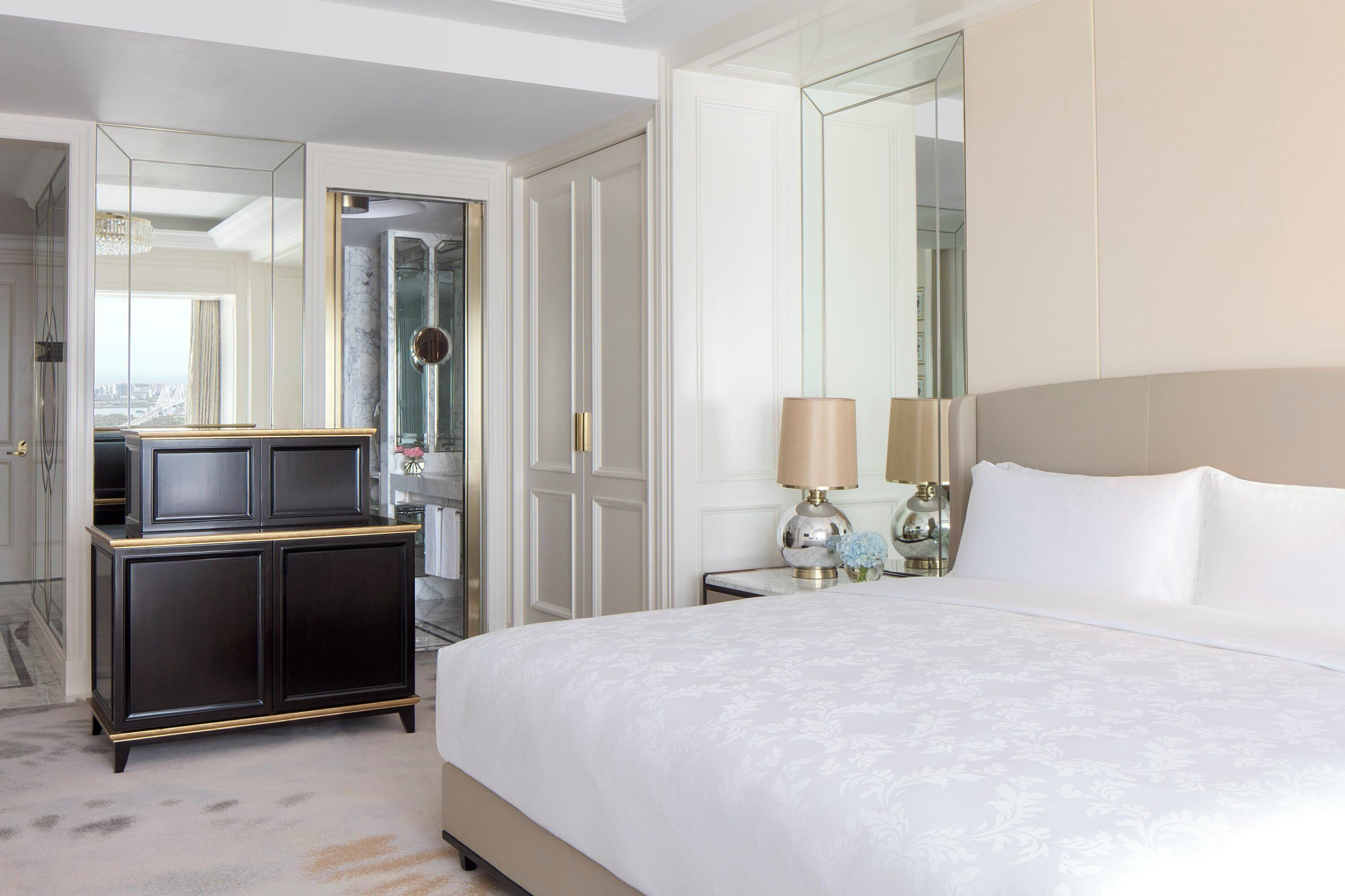 Habitación de hotel con una cama grande, un tocador, un espejo y una mesita de noche con lámparas.