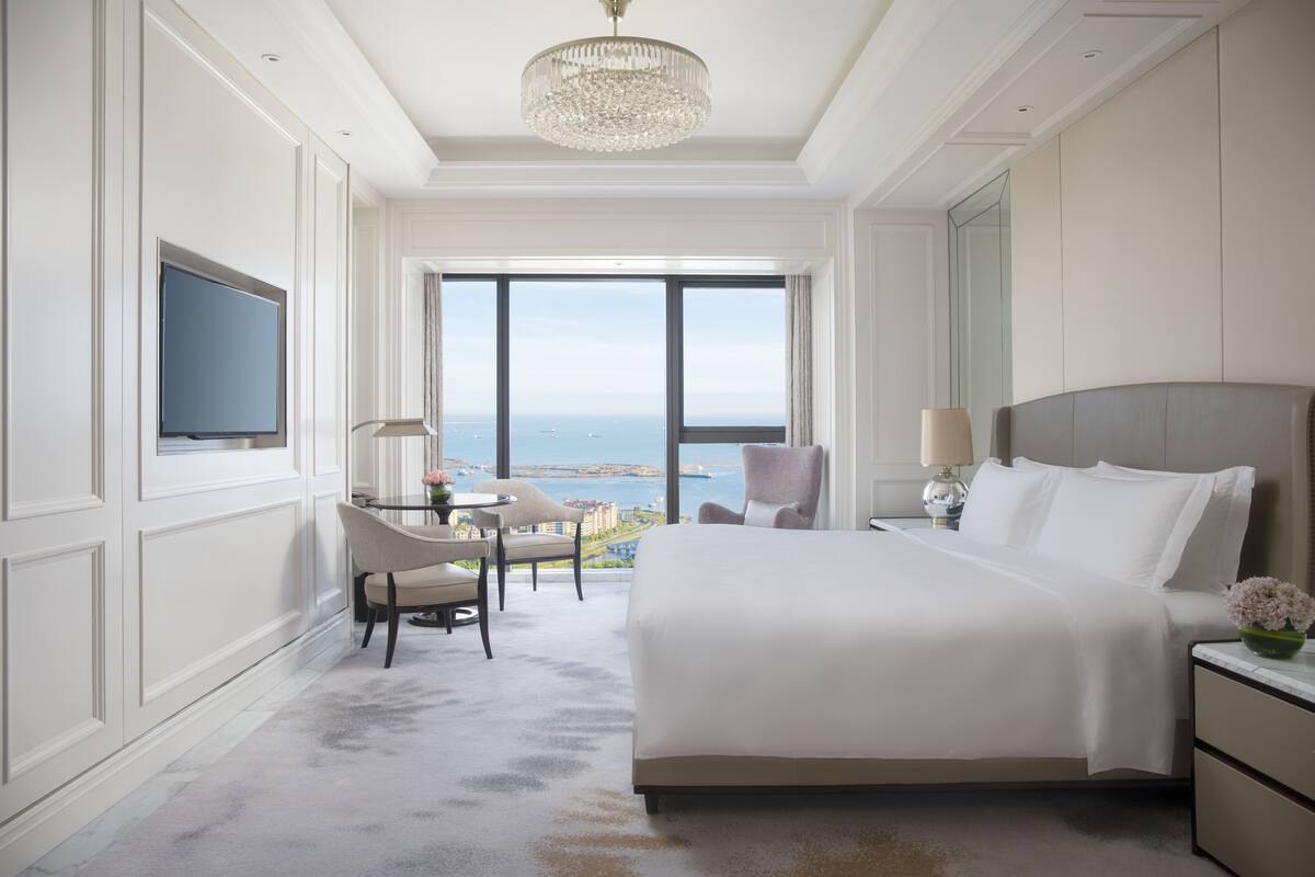 A hotel room with a large bed, a television, a desk with a chair, and a view of the sea.