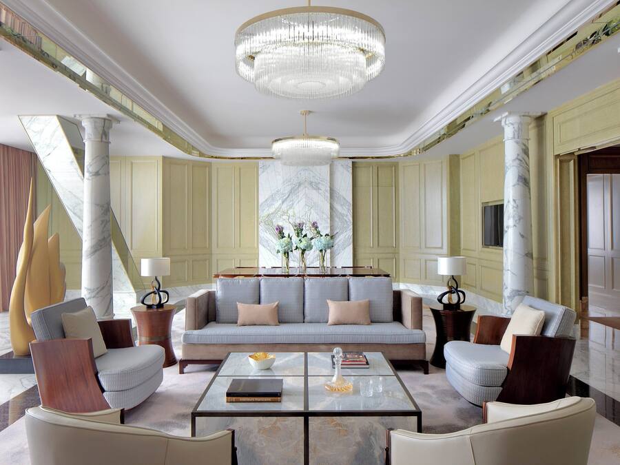 Um hall luxuoso com um imponente candelabro, colunas de mármore, um sofá macio e móveis elegantes.