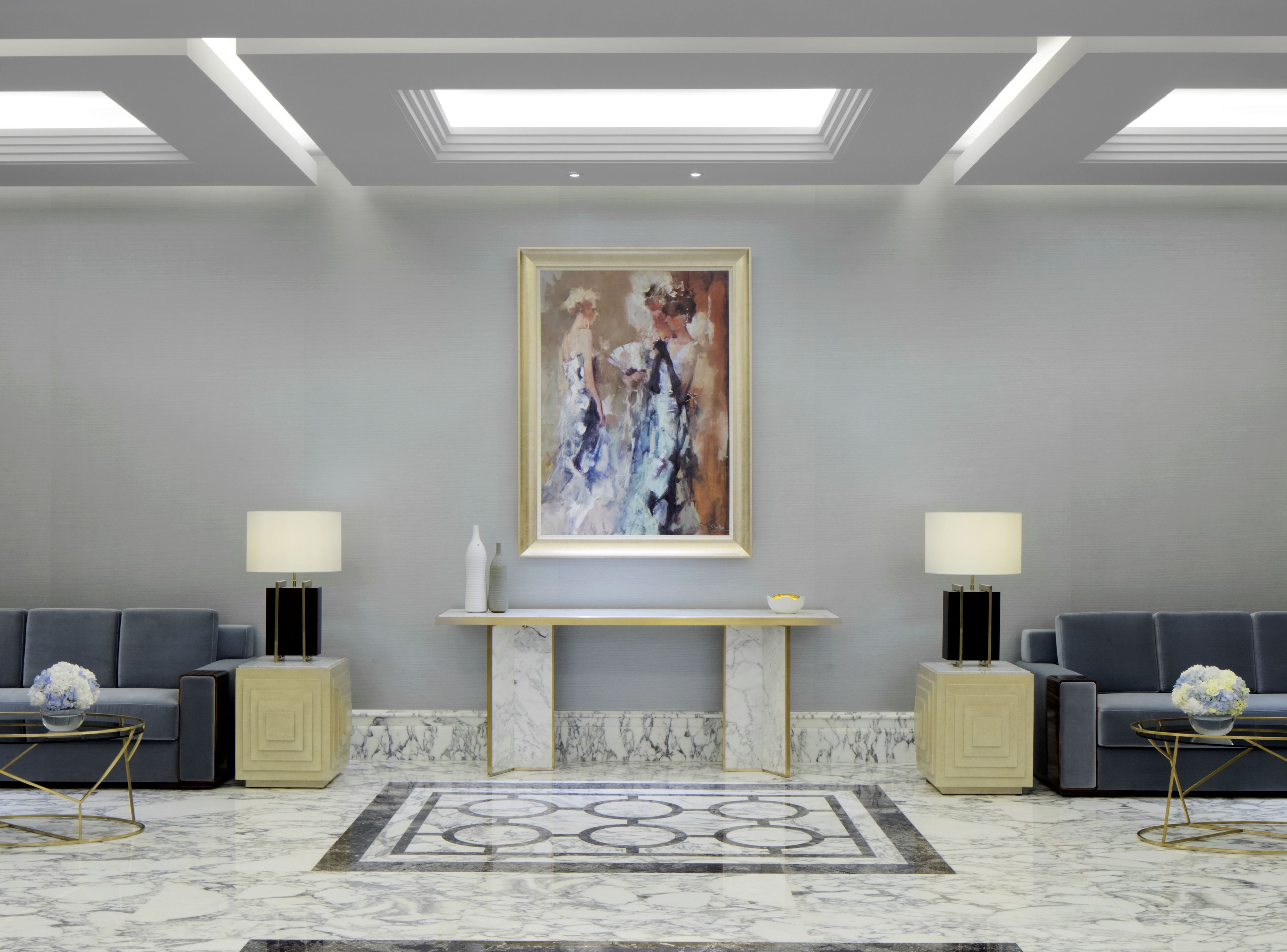 A modern lobby with a marble floor, a central console table, two sofas, and a large abstract painting on the wall.