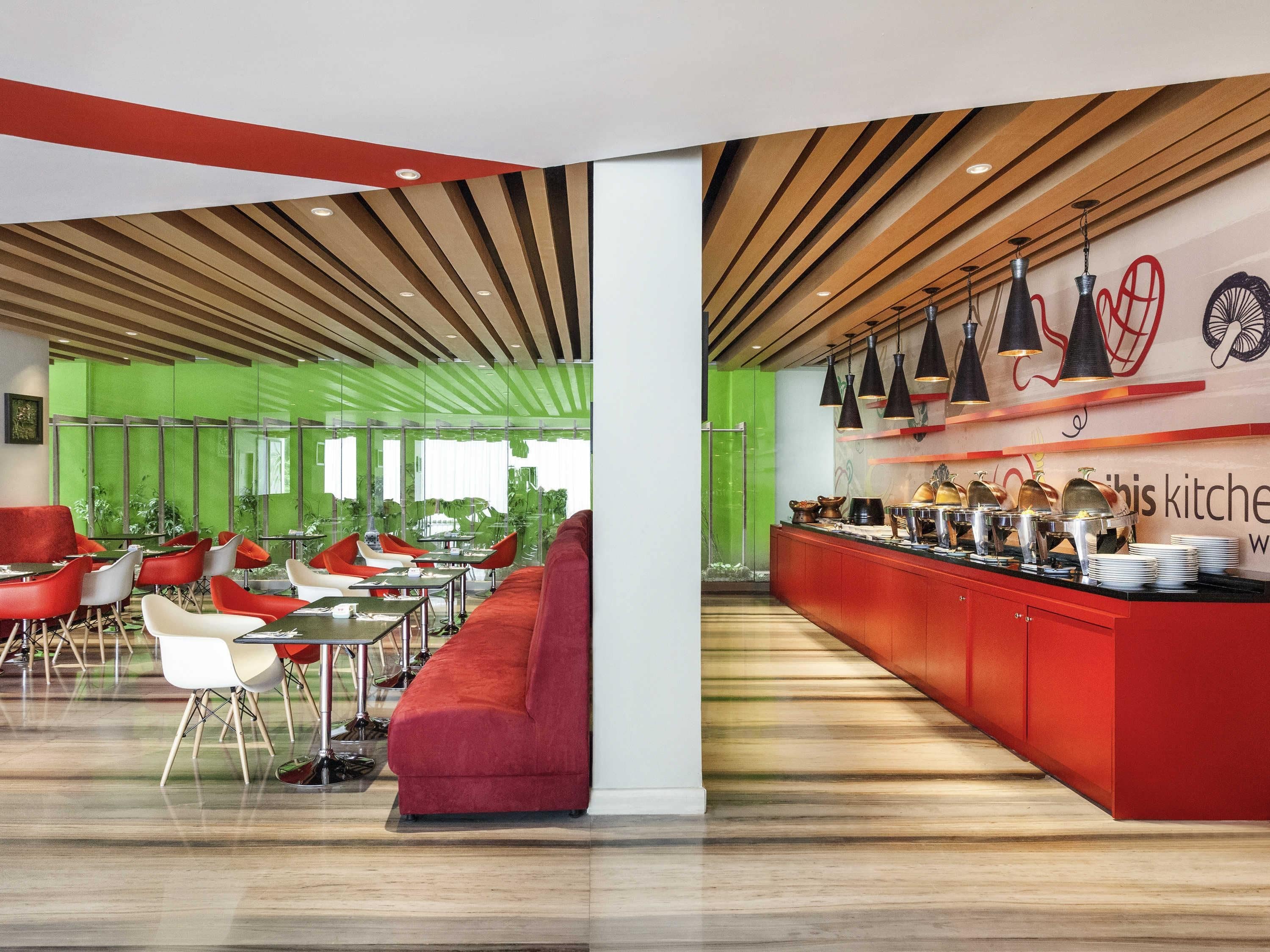 A modern interior with a red sofa, white and red chairs, a long counter with kitchenware, and a green wall.