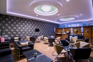 A modern hotel lobby with a patterned wall, a chandelier, and a bar area.