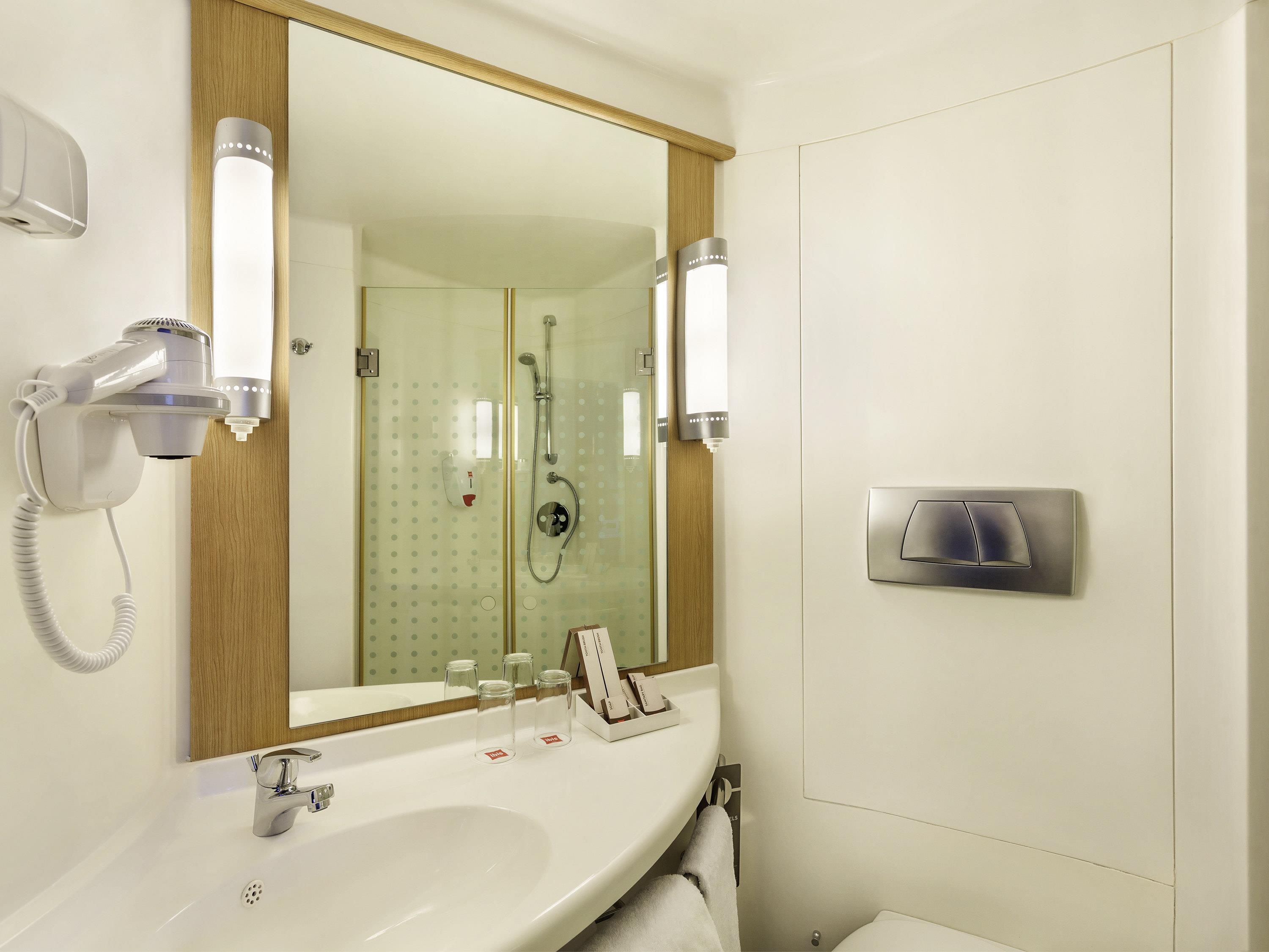 A bathroom with a large mirror, a sink, a hairdryer, and a shower.