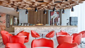 A modern restaurant interior with red chairs, a counter with food items, and a unique ceiling design.