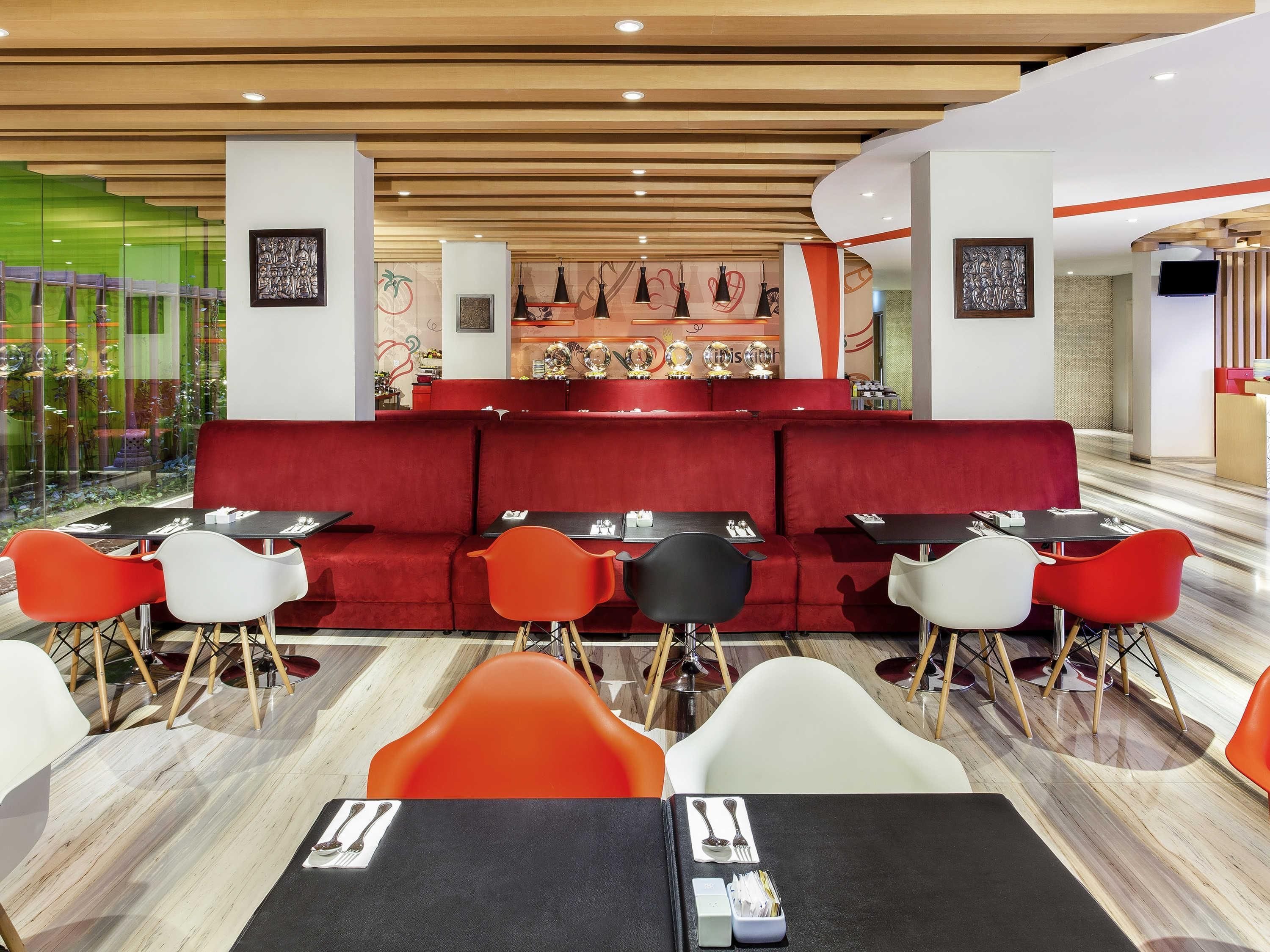 A modern restaurant with red seating, black tables, and a central bar area.