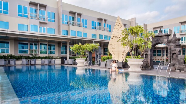 A swimming pool with a tiled floor, surrounded by lounge chairs and potted plants.