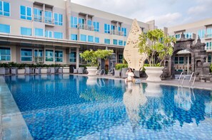 A swimming pool with a tiled floor, surrounded by lounge chairs and potted plants. - ibis Yogyakarta Adi Sucipto (Yogyakarta)