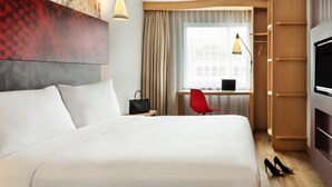 A hotel room with a large bed, a desk with a laptop, a red chair, a TV, and a wardrobe.