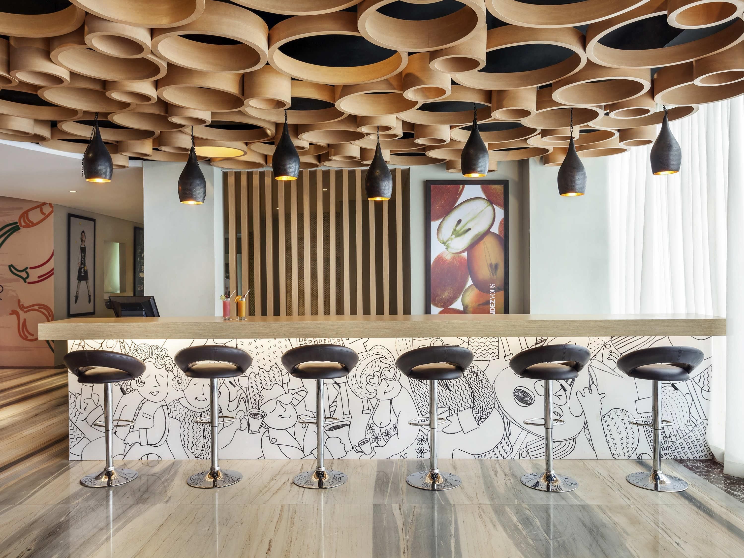 Un espace bar doté d’un plafond en bois, de luminaires suspendus noirs et d’un comptoir avec des tabourets.