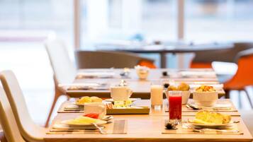 Une table mise pour le petit-déjeuner, avec des tables, des chaises et divers aliments et boissons.