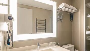 Une salle de bain moderne avec un grand miroir, un lavabo, un porte-serviettes et des toilettes.