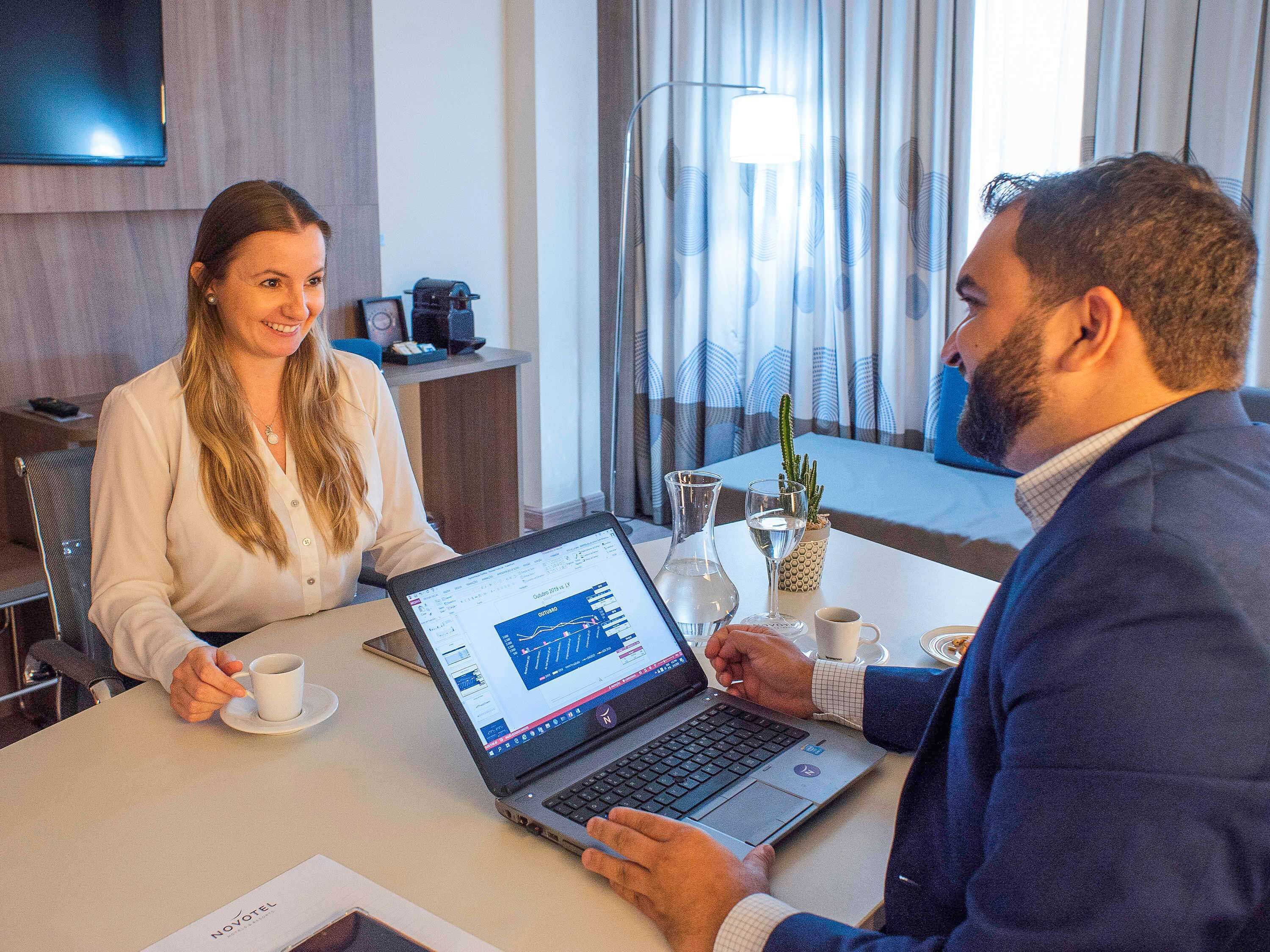 A hotel room with a laptop on a table, a coffee cup, a wine glass, and a cactus plant.