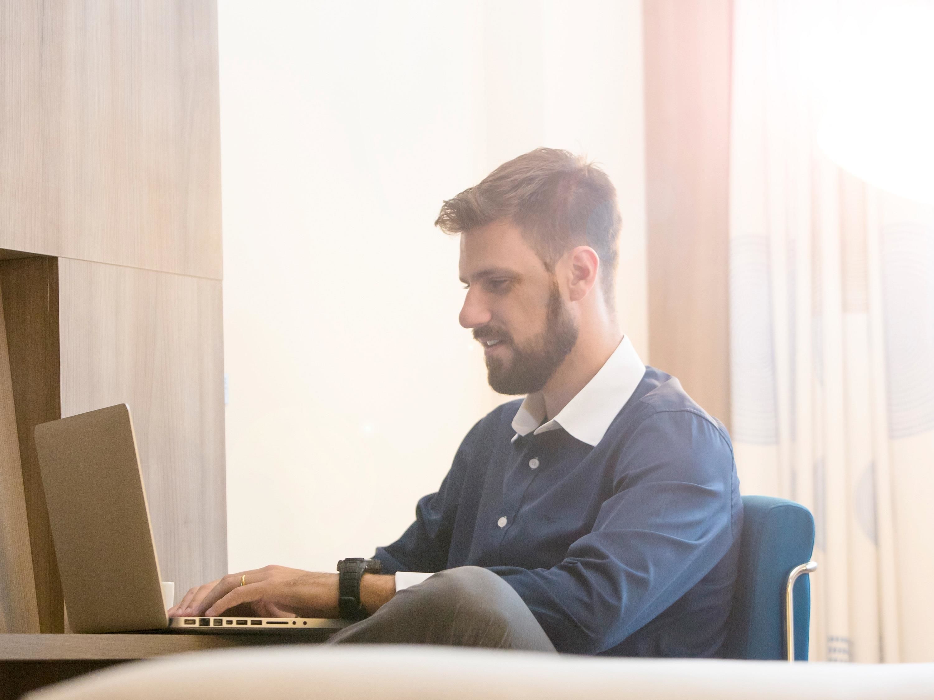 Una persona sentada a una mesa con una computadora portátil en una habitación moderna con paneles de madera y un ventanal grande.
