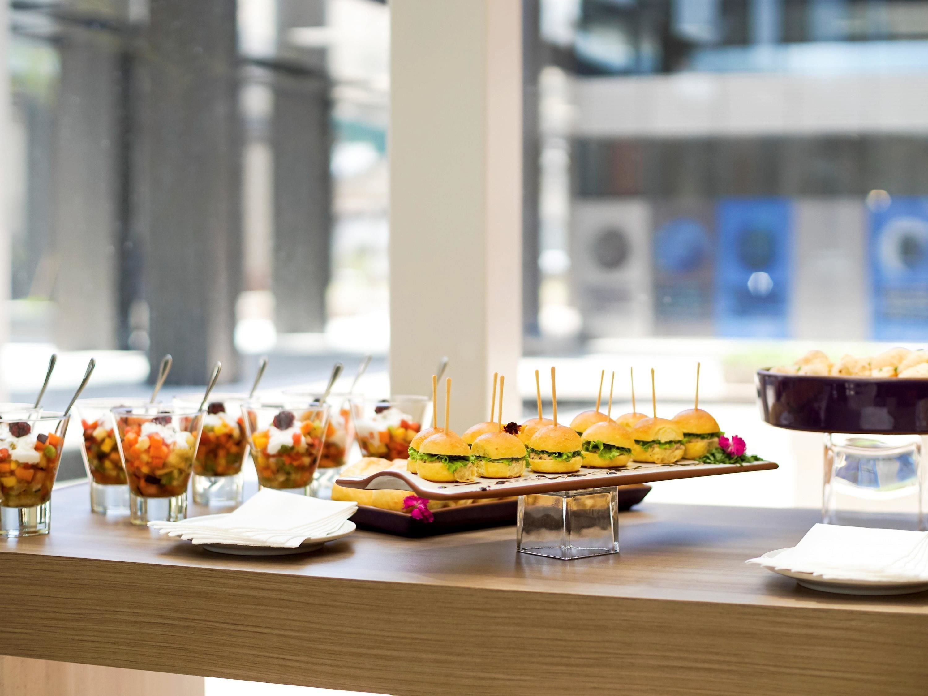 A buffet table with various food items, including a tray of sandwiches and small cups of salad.